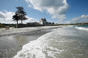 A beach with a large building in the background, a tree, and people walking along the shore. - Apartment in Plougasnou with Sea Views (Plougasnou)