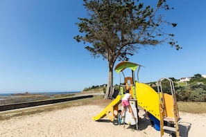 A playground with climbing structures and a slide, located on a sandy beach with a clear view of the sea in the background. - Apartment in Plougasnou with Sea Views (Plougasnou)