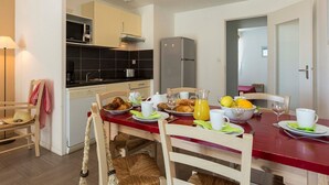 A compact kitchen with modern appliances, a dining area with breakfast setup, and a visible door leading to another room.