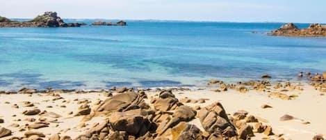 Uma praia rochosa com águas azul-claras e formações rochosas ao longe.