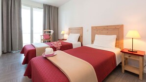 A hotel room with two beds, a chair, a lamp, and a window with curtains.