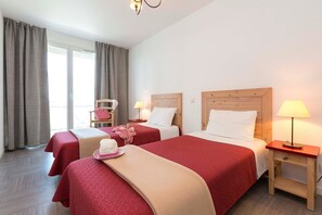 A hotel room with two beds, a chair, a lamp, and a window with curtains.