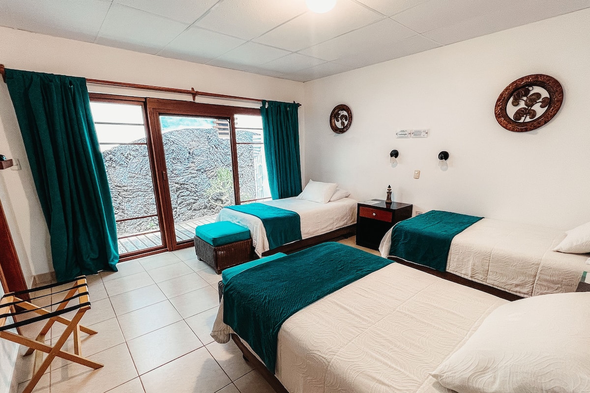 A hotel room with two beds, a wooden chair, a small table, and a window with curtains.