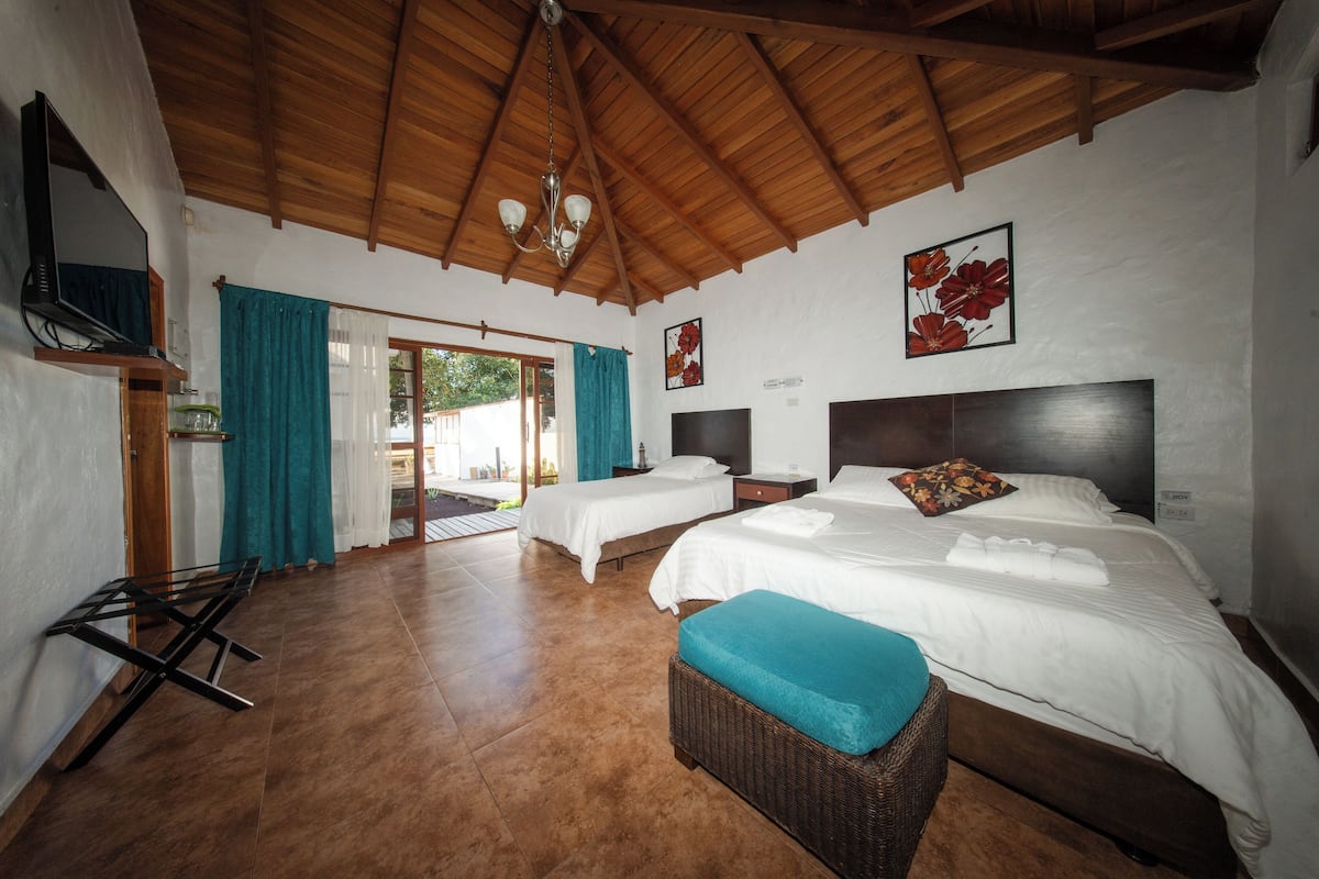 A hotel room with two beds, a TV, a ceiling fan, and a view of the outdoors.