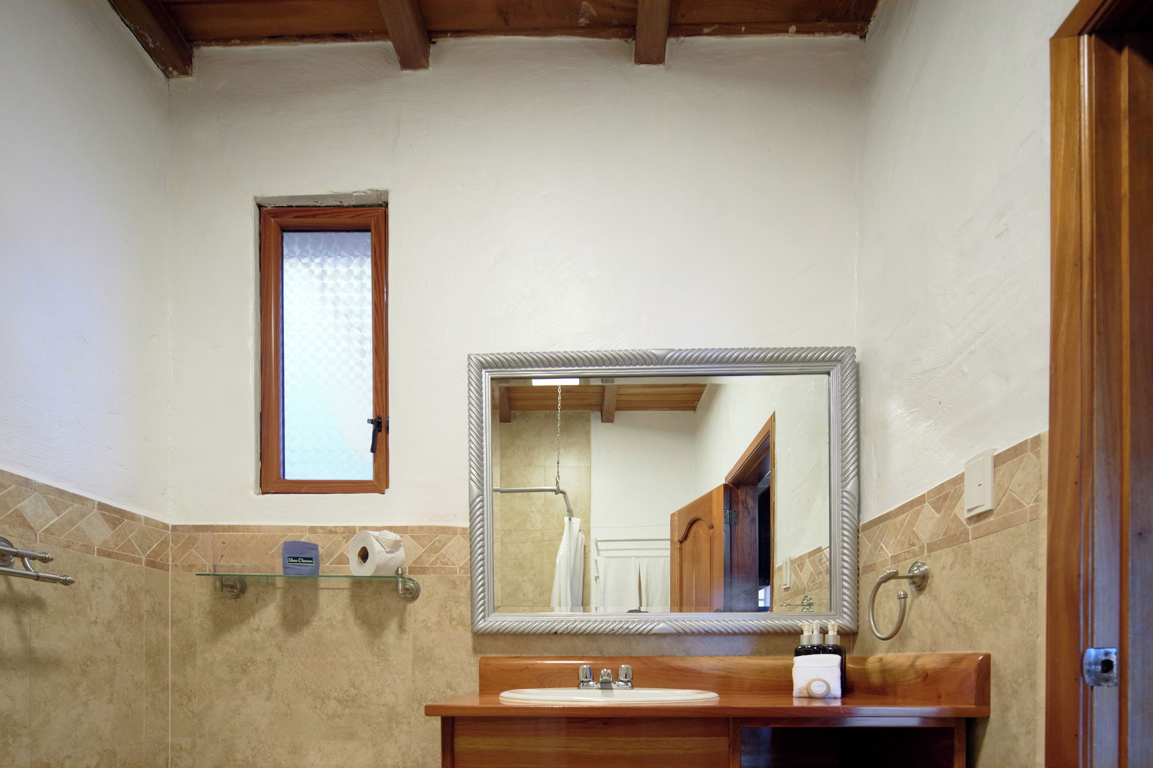 A bathroom with a wooden vanity, a large mirror, a towel rack, and a window.