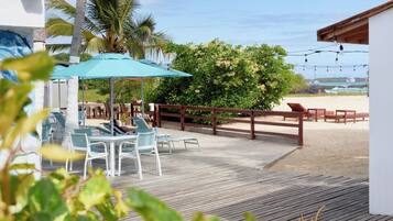 A wooden deck with outdoor seating, a view of the beach, and a palm tree.