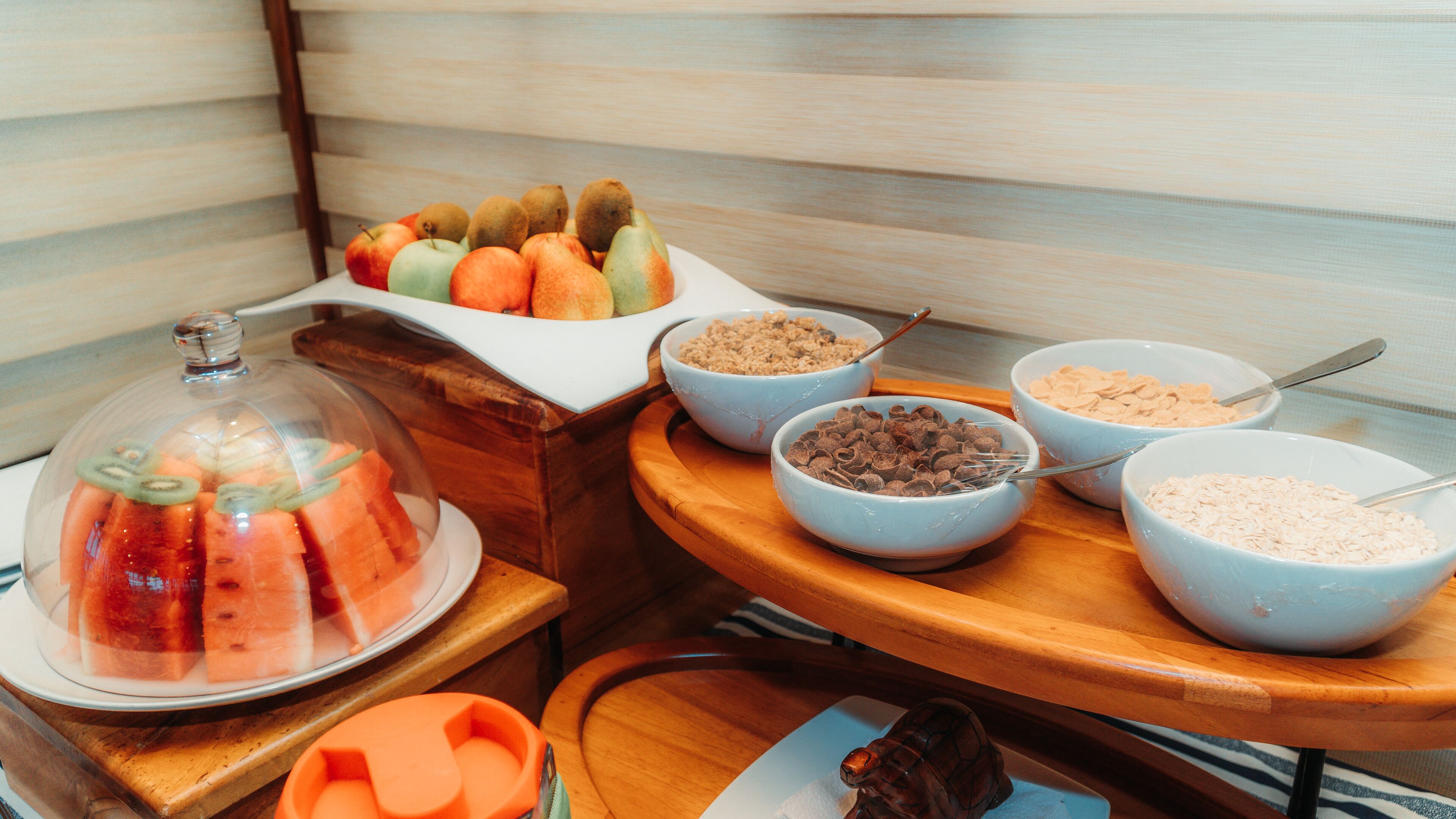 A breakfast buffet with various fruits, cereals, and a covered fruit display.