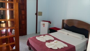 Een hotelkamer met een houten bedframe, een kleine witte koelkast en een rode tafel.