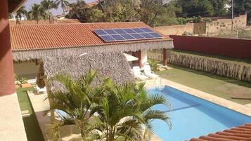 A pool area with a thatched-roof structure, solar panels, and palm trees.