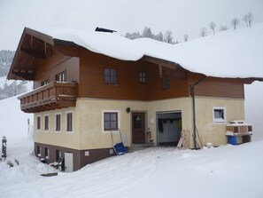 A two-story wooden chalet with a balcony, a door, and a small window.