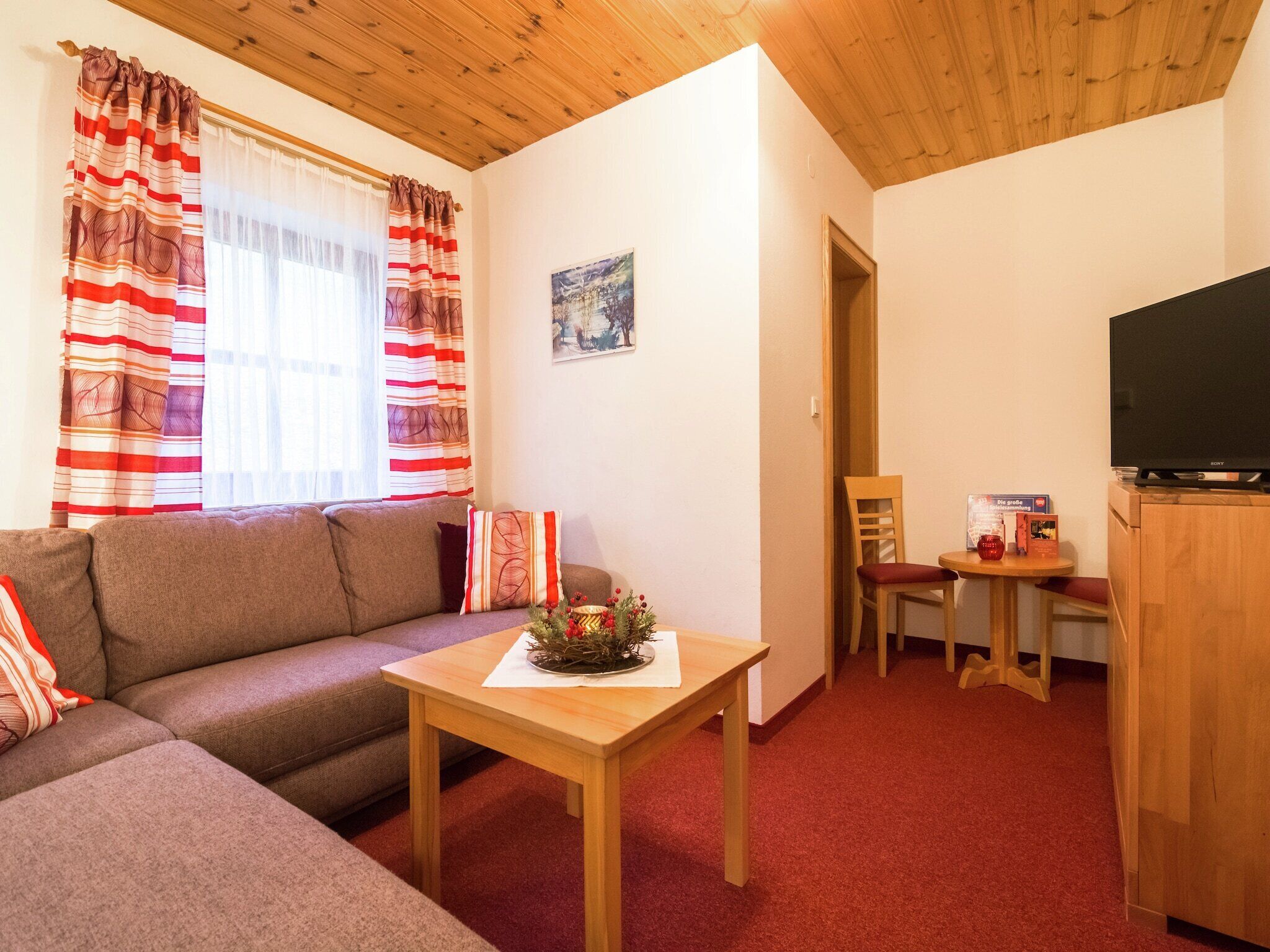 Een gezellige woonkamer met een bank, een houten tafel met een decoratief middelpunt, een televisie op een houten kast, en een eethoek met een stoel en tafel.