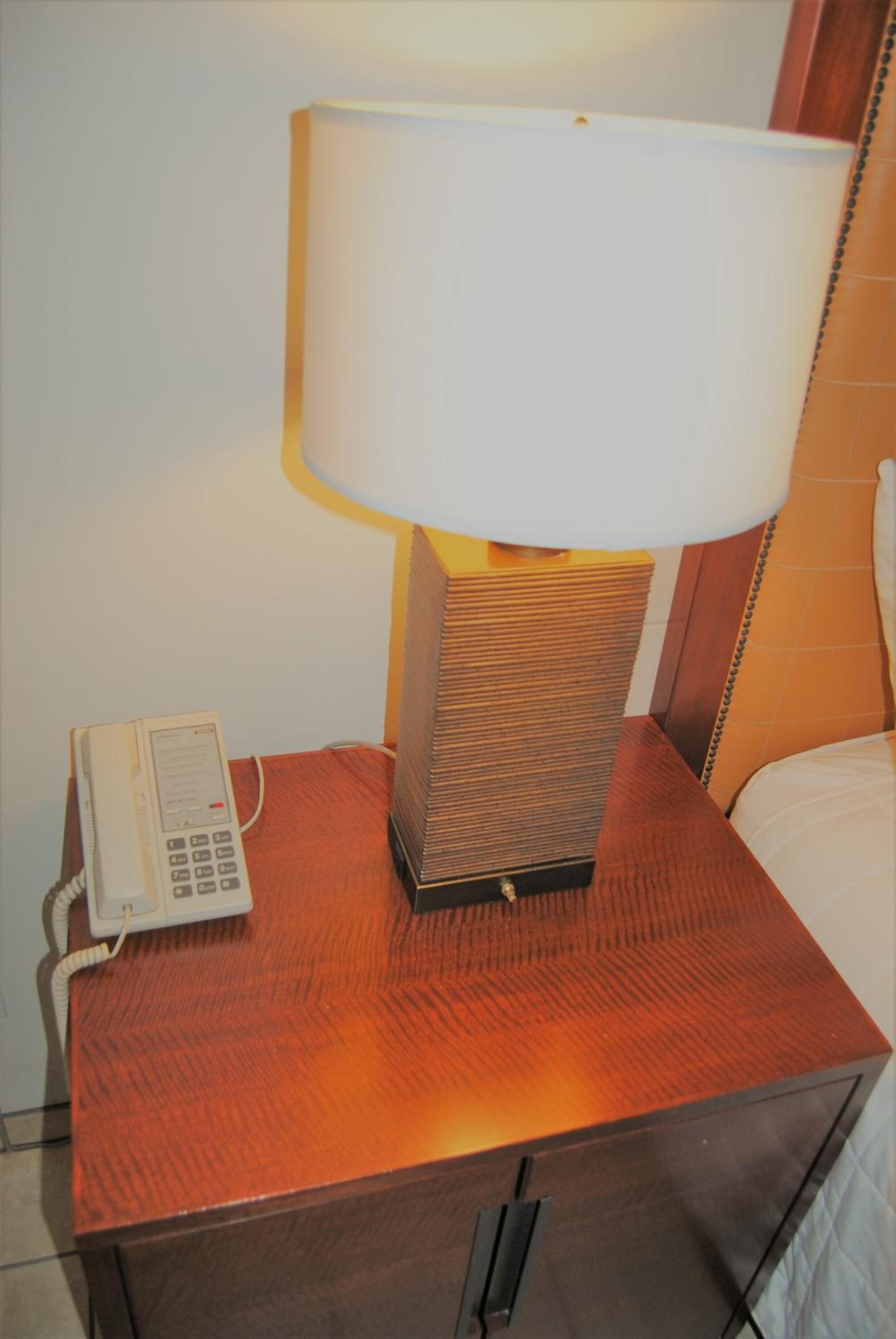 Een houten nachtkastje met een lamp en een telefoon.
