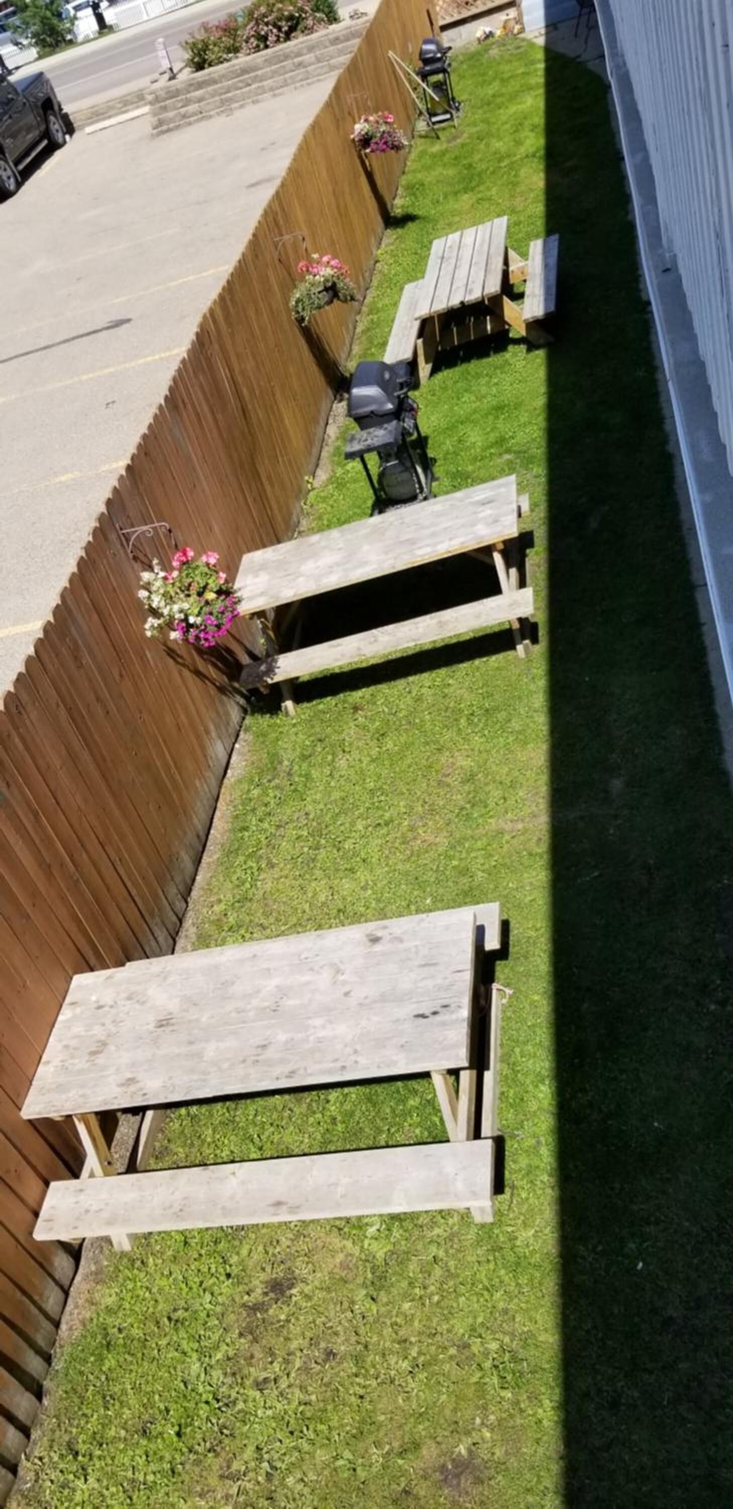 A row of wooden picnic tables and benches along a wooden fence with flower planters.