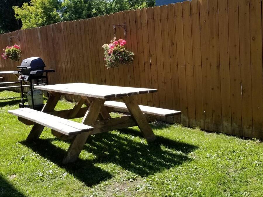 A picnic area with wooden tables and benches, a barbecue grill, and hanging flower baskets.