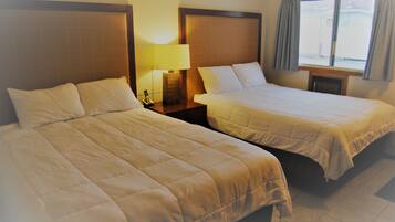 A hotel room with two beds, a nightstand with a lamp, and a window with curtains.
