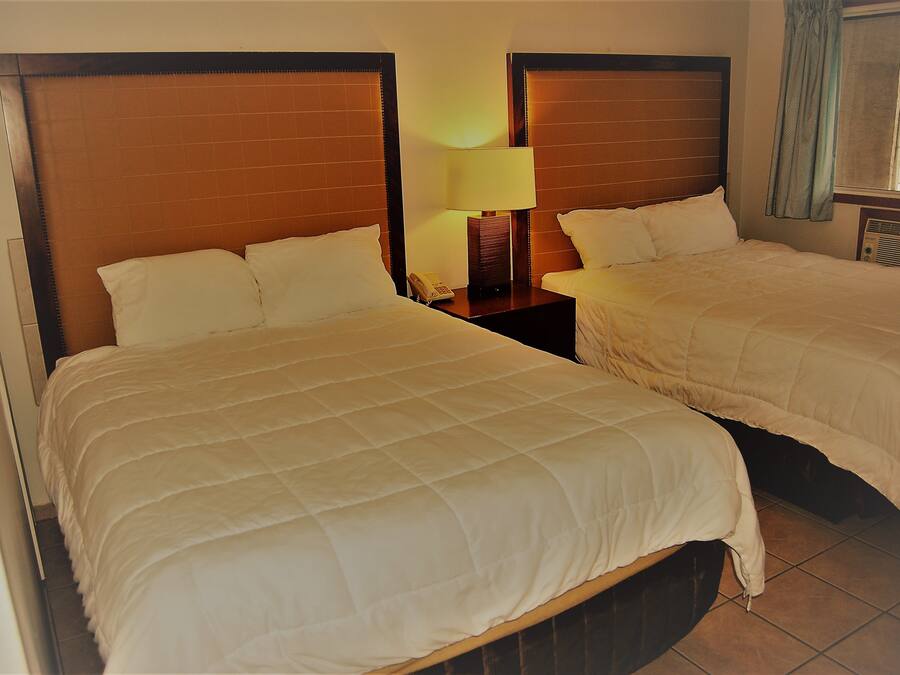 A hotel room with two beds, a nightstand with a lamp, and a window with curtains.
