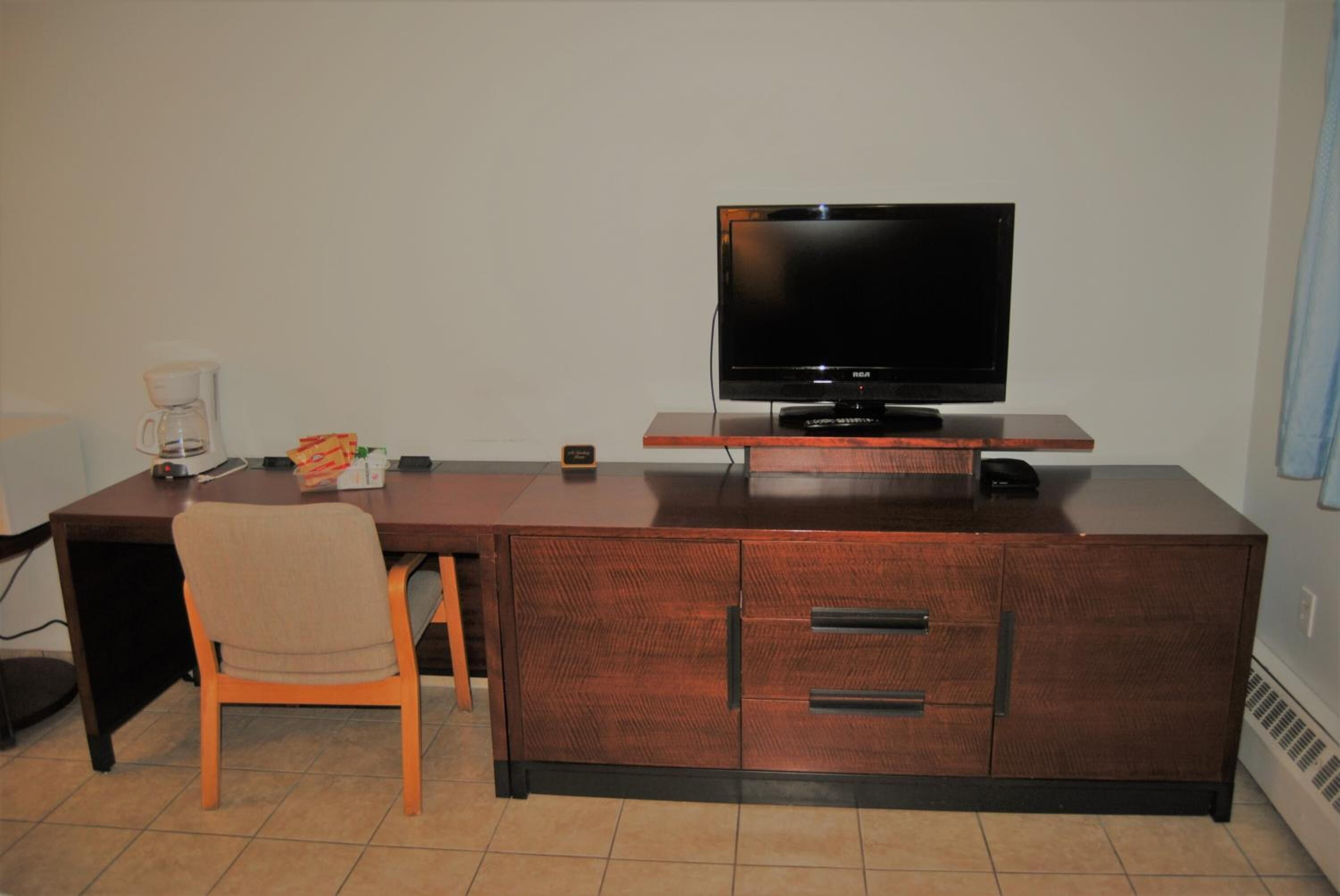 A hotel room with a wooden desk, a television, a chair, and a coffee maker.