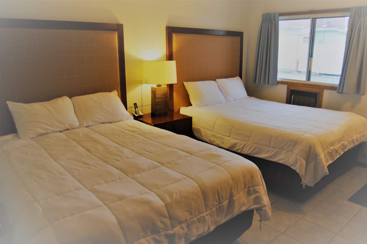 Two single beds with headboards, a bedside table with a lamp, and a window with curtains.