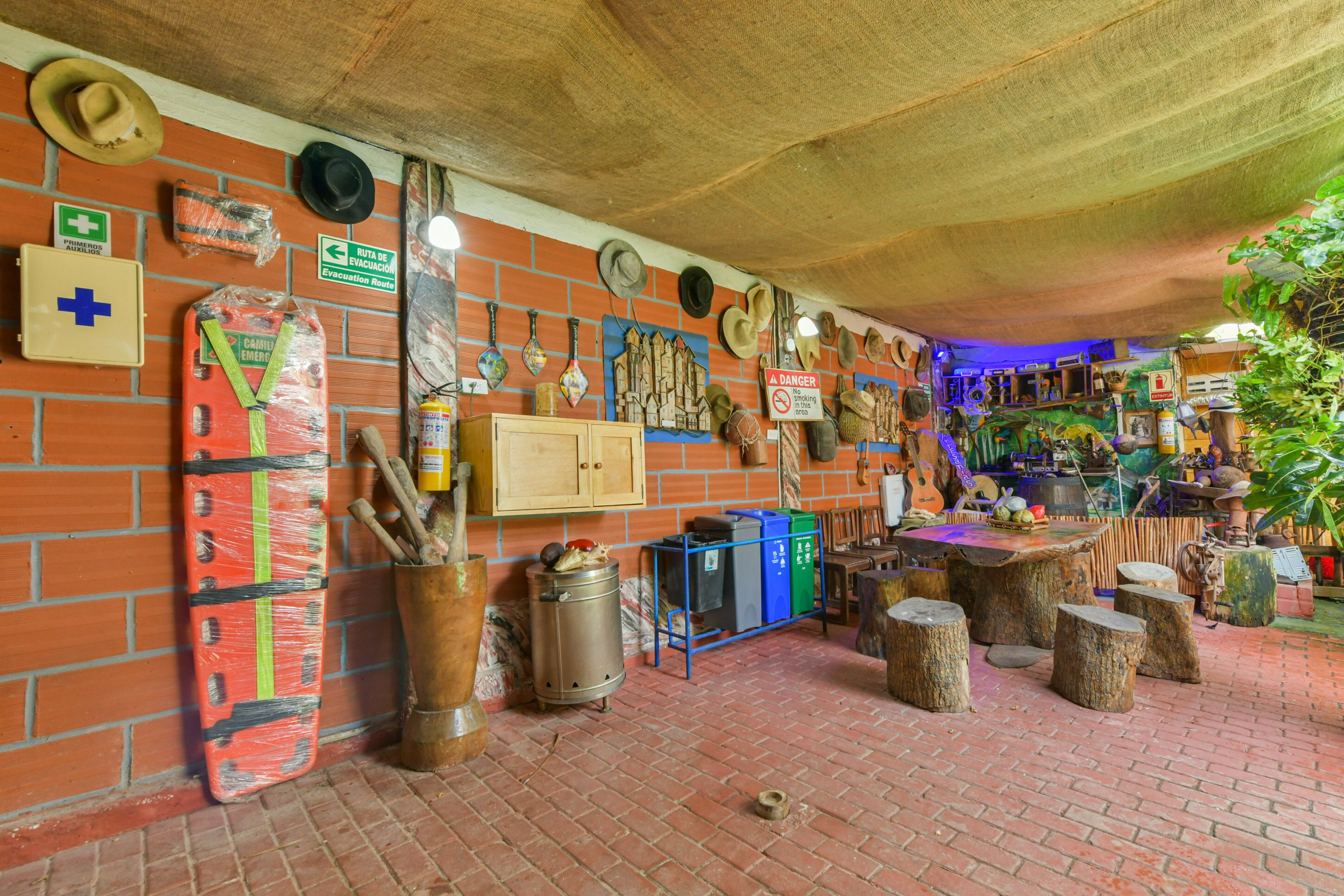 Interior rústico com parede de tijolos, equipamentos de emergência e diversos chapéus e ferramentas expostos.