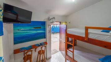 Una habitación con una cama litera, un escritorio con dos sillas, un televisor montado en la pared y un cuadro de una playa.