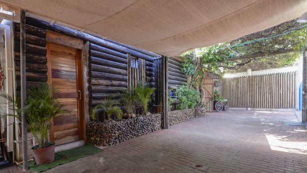 A log cabin with a wooden door, potted plants, and a brick pathway leading to a covered area.
