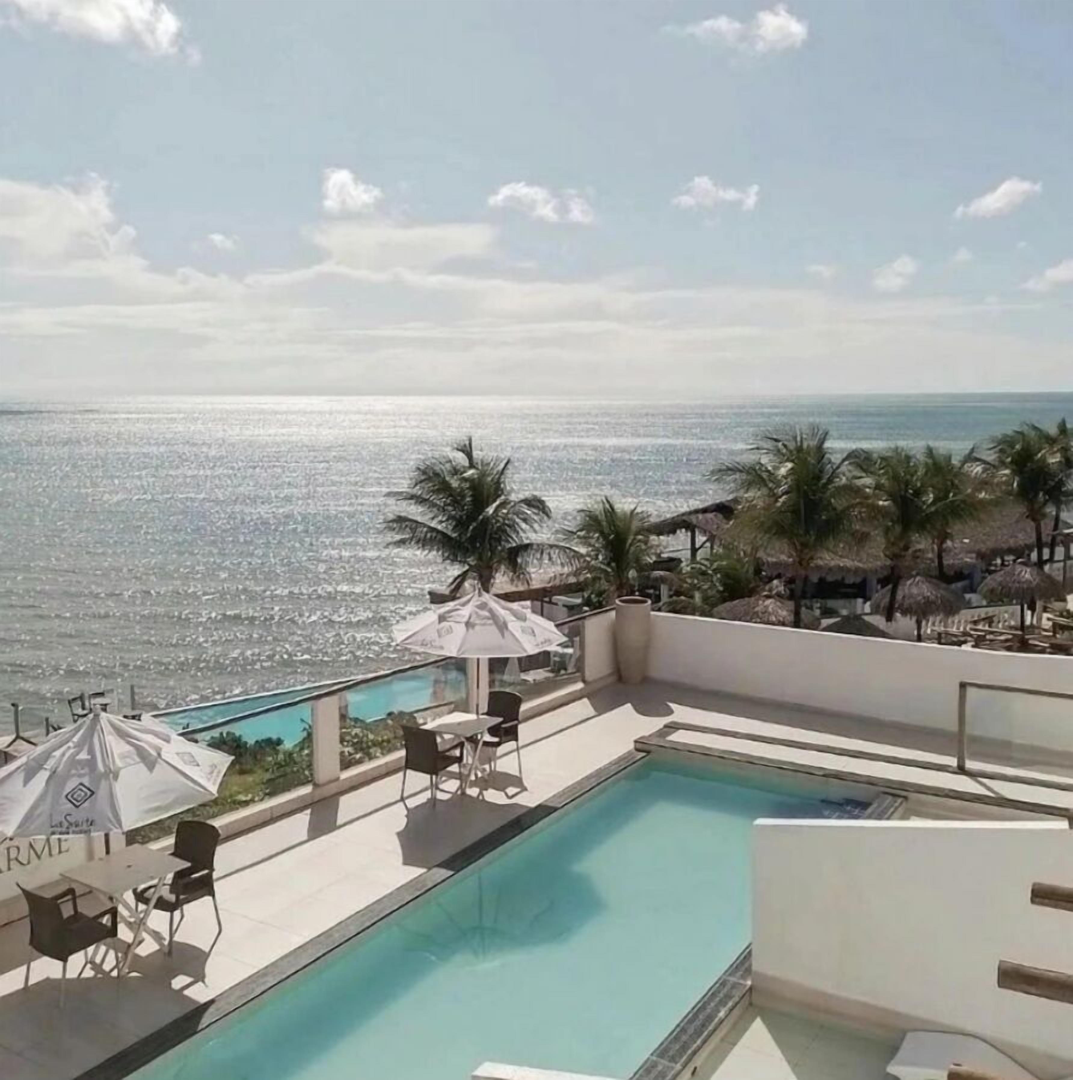 Une piscine sur le toit, offrant une vue sur l’océan, entourée de palmiers et de parasols.