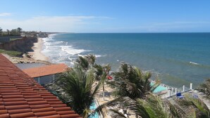A coastal view with a beach, ocean, and a pool area with palm trees. - La Suite Praia Hotel (Caucaia)