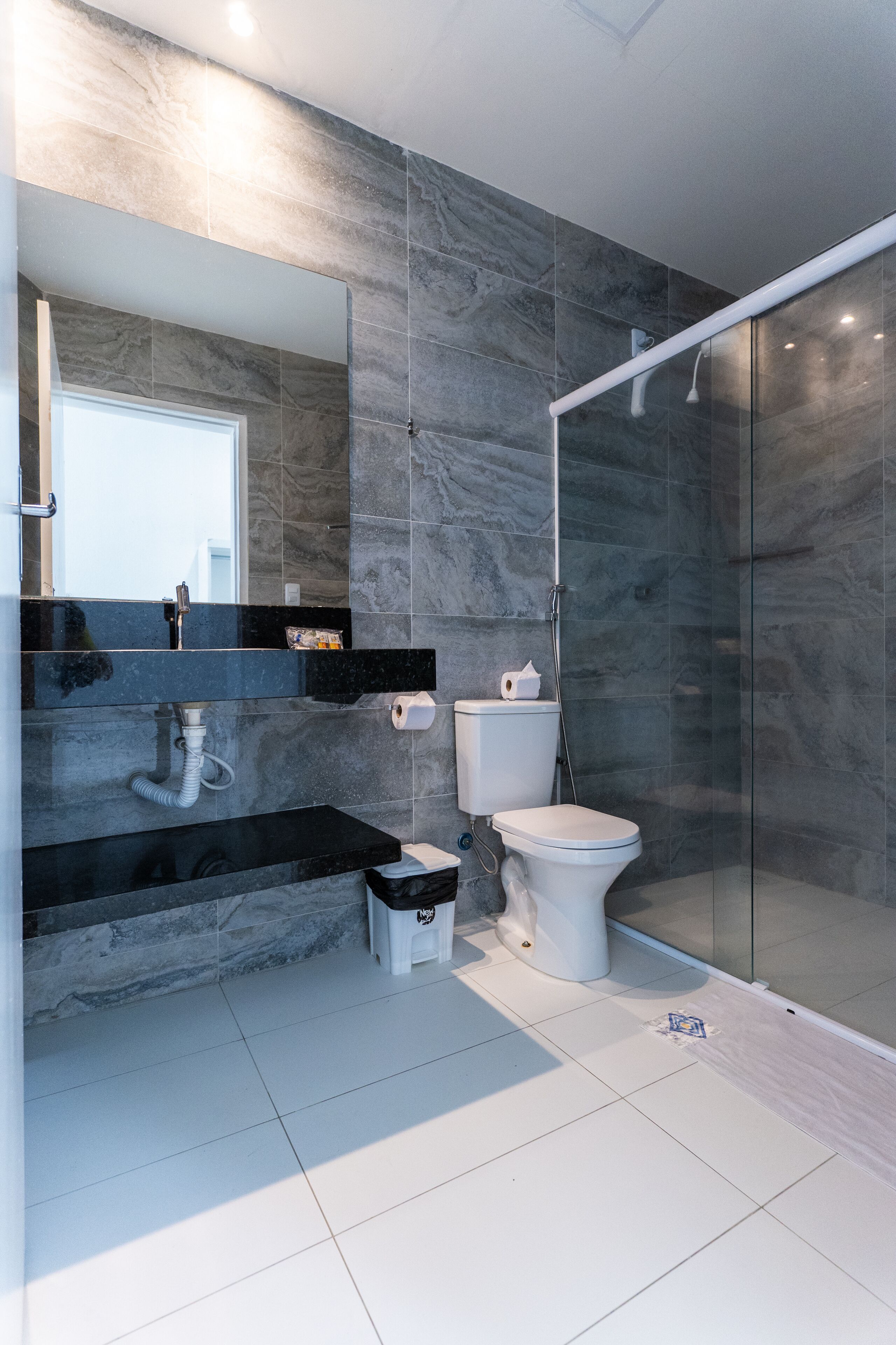 Un baño moderno con cabina de ducha de vidrio, tocador negro y salpicadero de mármol.