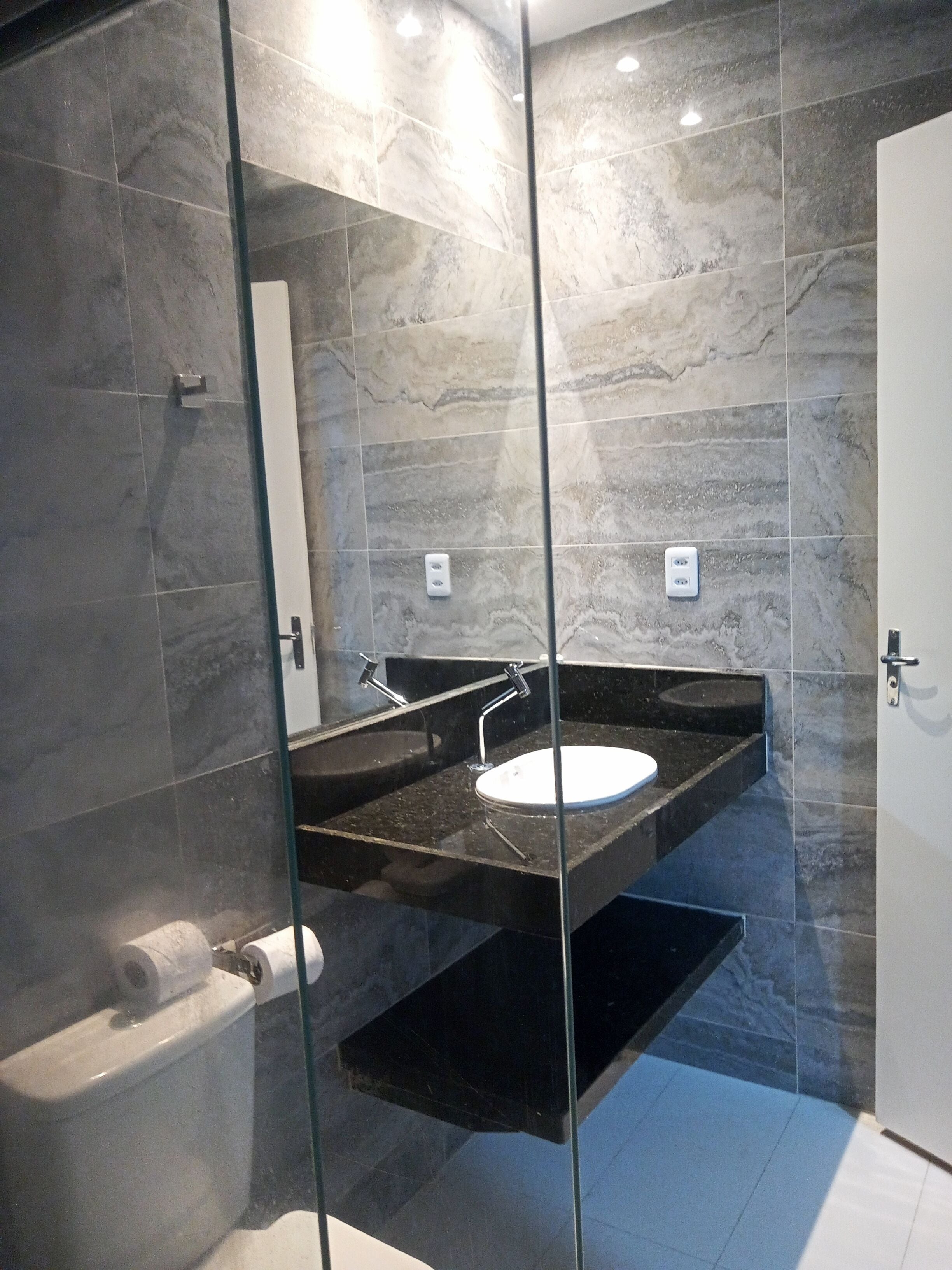A modern bathroom with a glass-enclosed shower, two sinks, and a toilet.