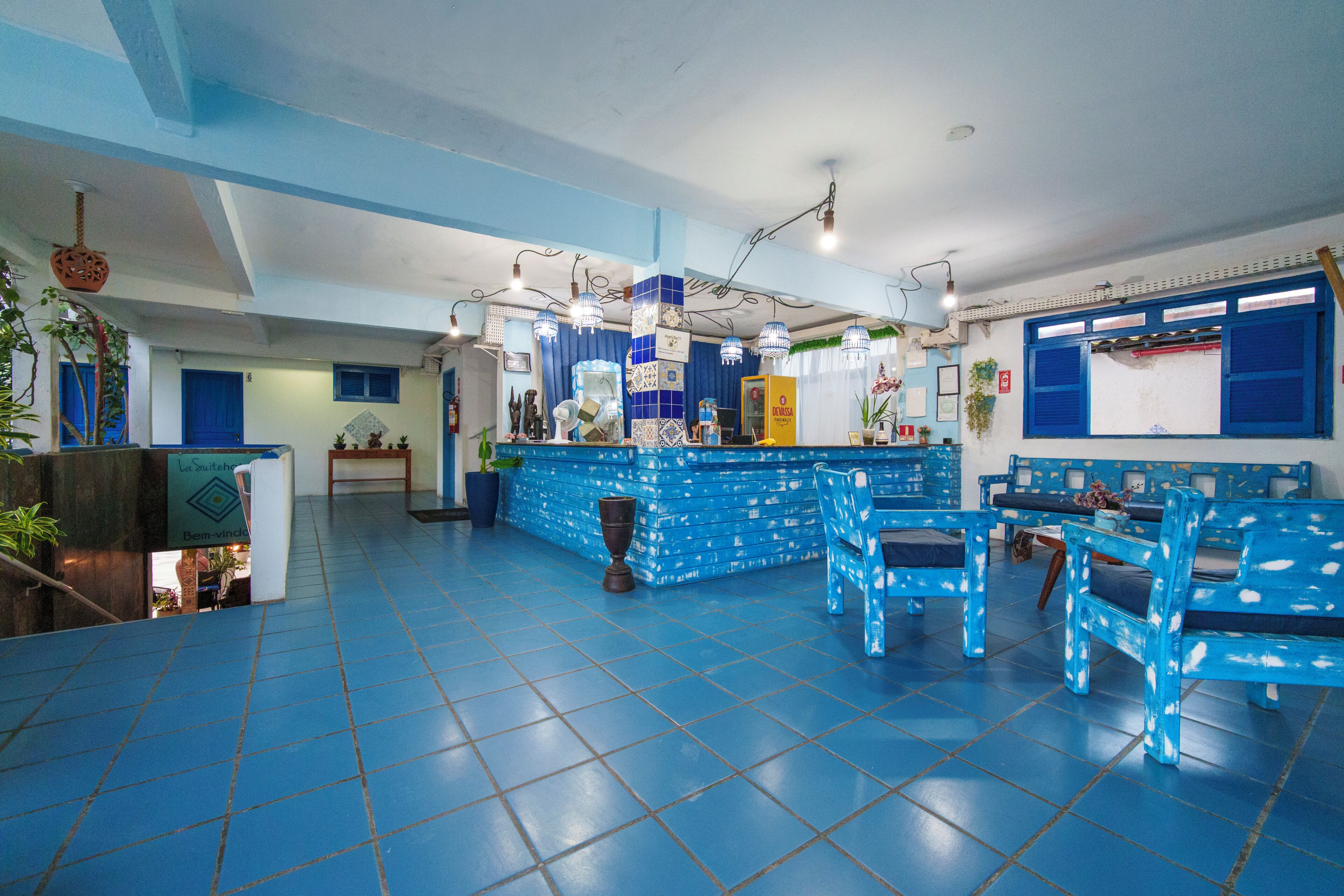 A hotel lobby with blue tiled floors, a reception desk, and blue patterned chairs.