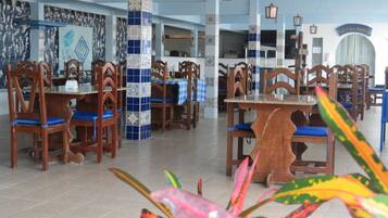 Un comedor con mesas y sillas de madera, cojines azules y una columna de azulejos.