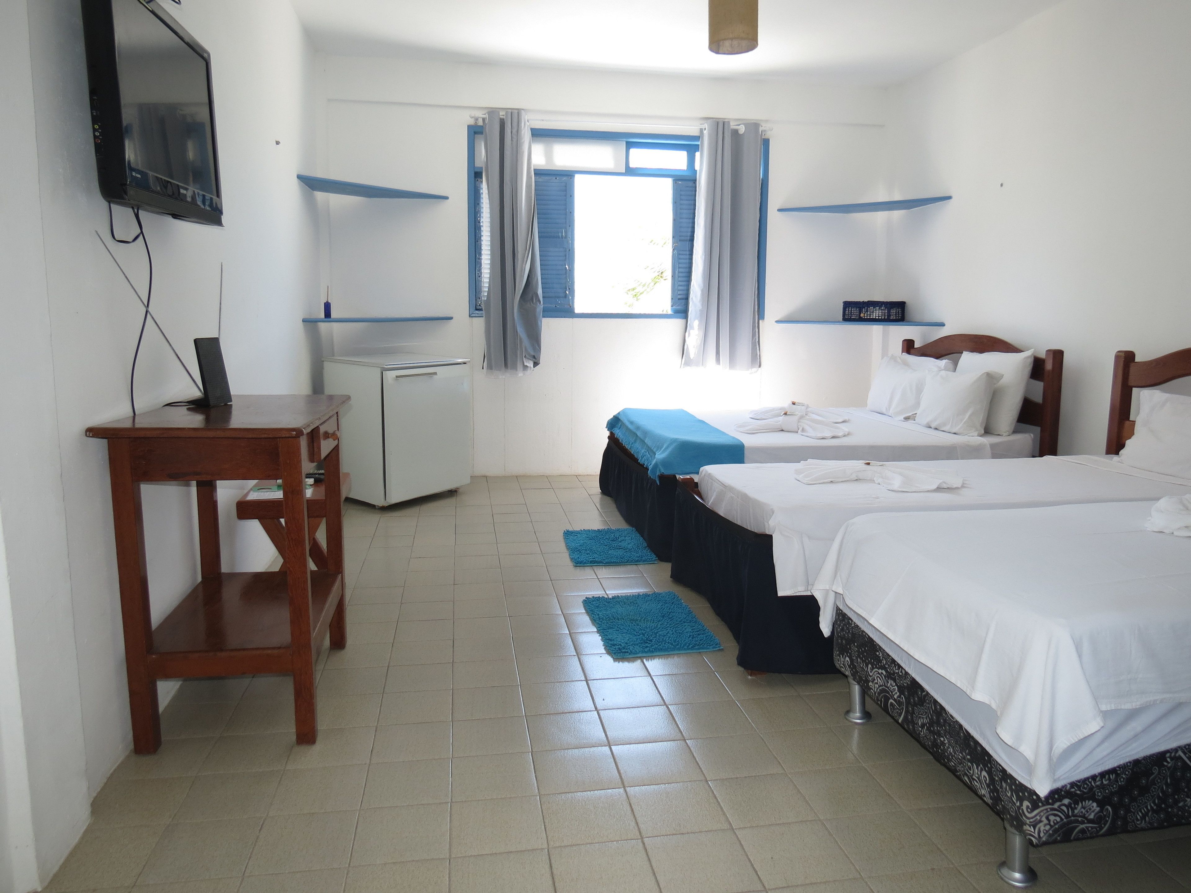 A hotel room with two beds, a desk, a small refrigerator, and a television mounted on the wall.