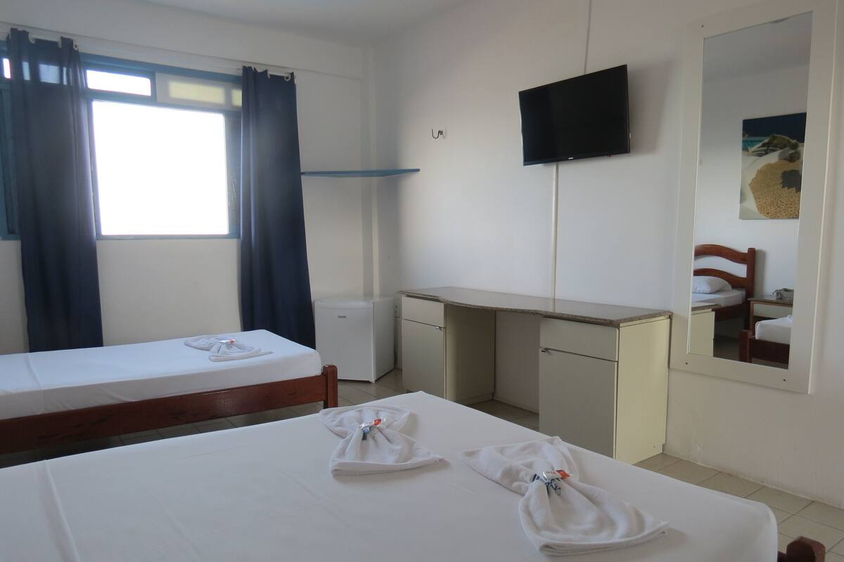 Hotellihuone, jossa on kaksi erillistä sänkyä, työpöytä, televisio ja pieni jääkaappi.