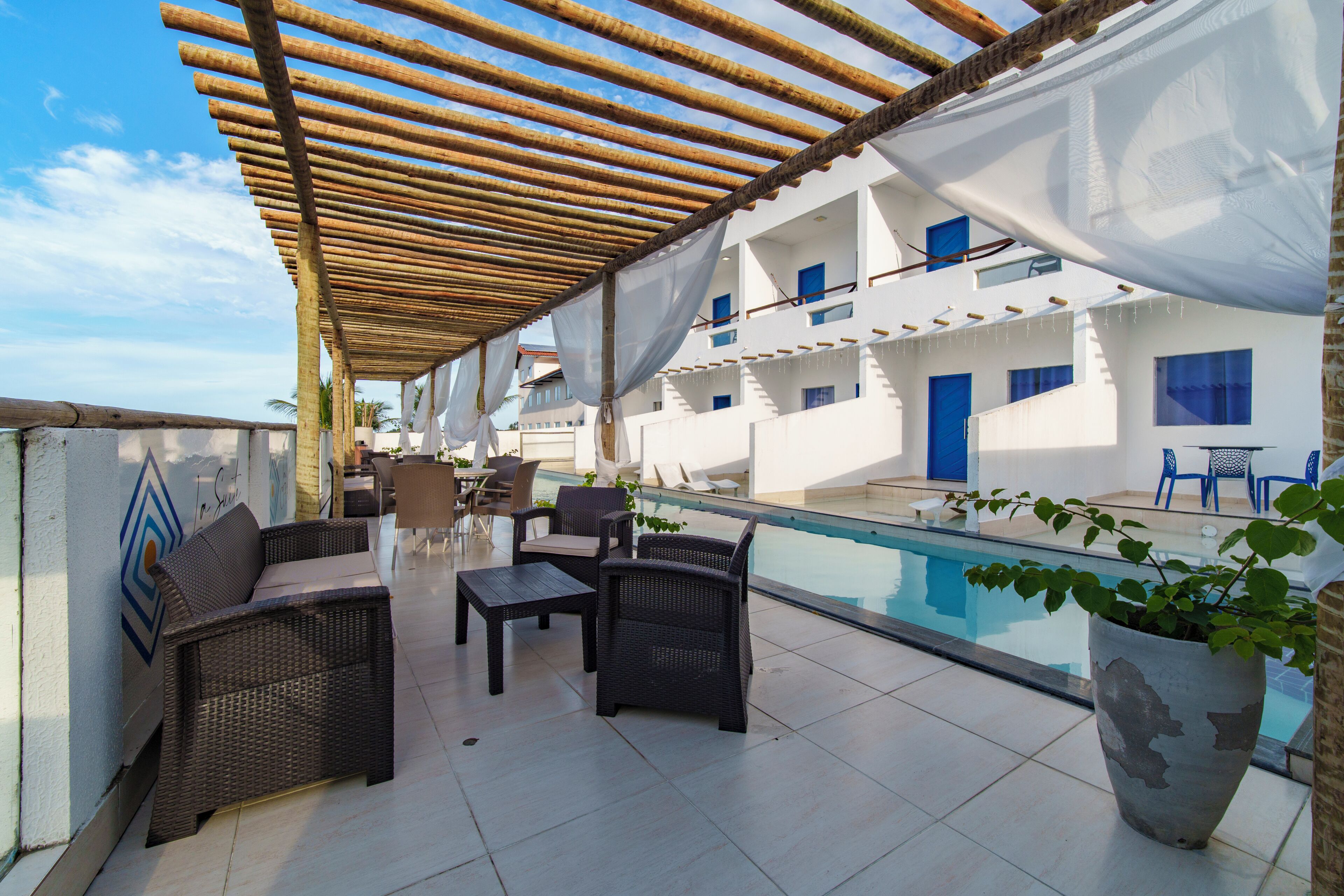 Una terraza en la azotea con mobiliario de mimbre, una piscina y un edificio con ventanas azules.