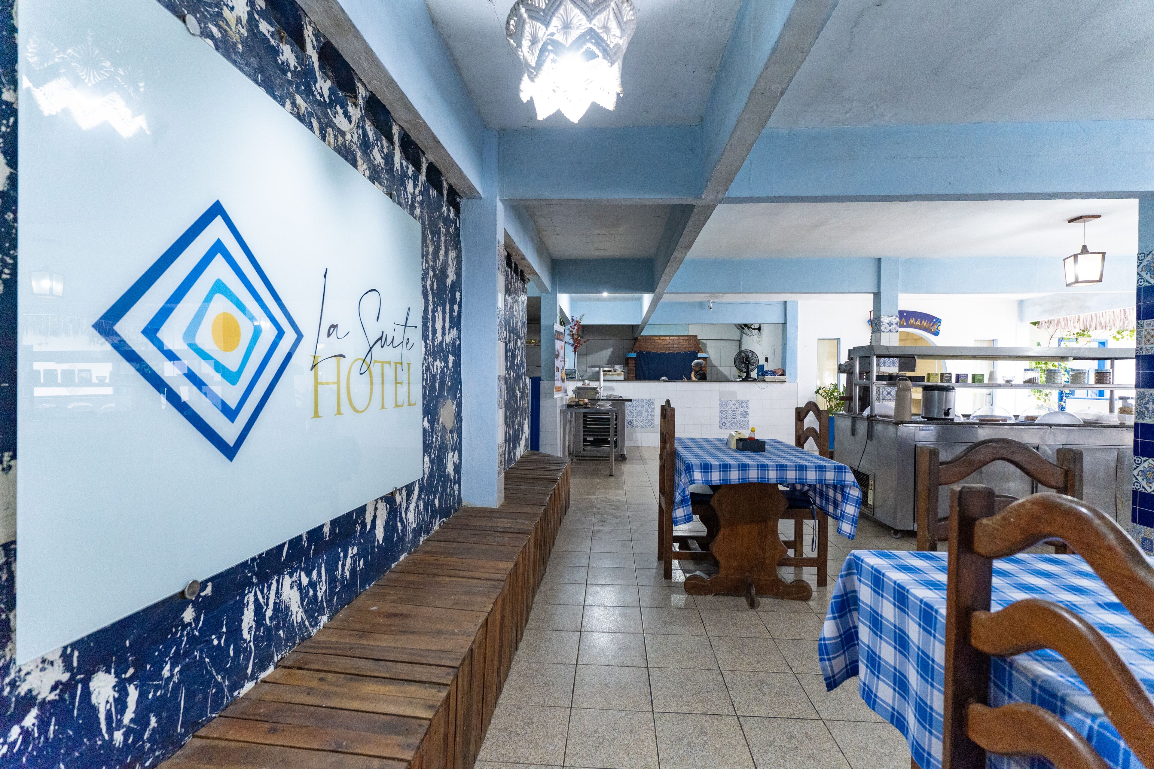 A restaurant with a blue and white color scheme, featuring a logo with a diamond shape and a sun. There are wooden benches and tables with blue checkered tablecloths.