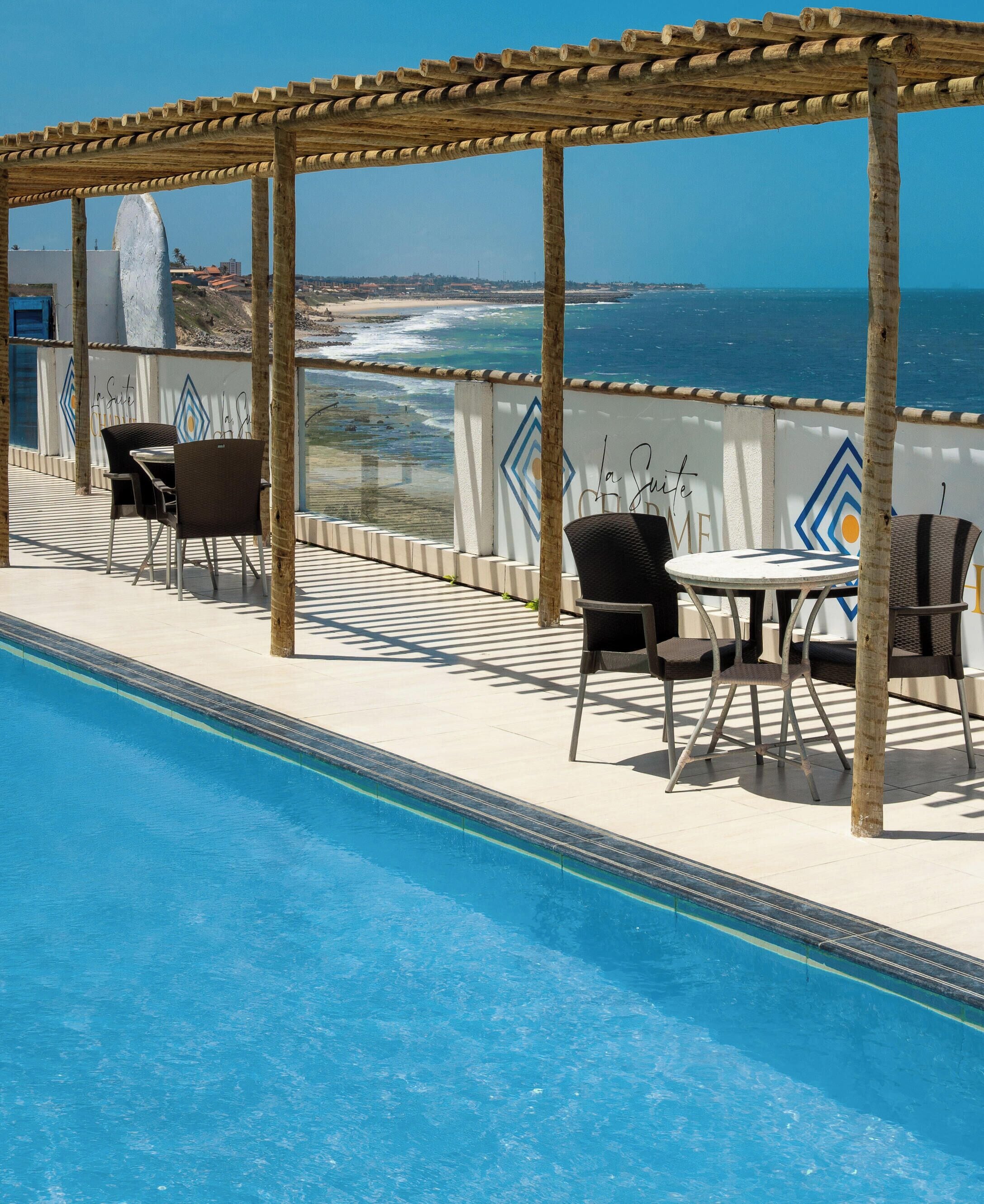 Zona junto a la piscina con una pérgola, sillas y vistas al océano.