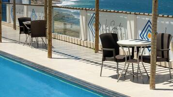 Zona junto a la piscina con una pérgola, sillas y vistas al océano.