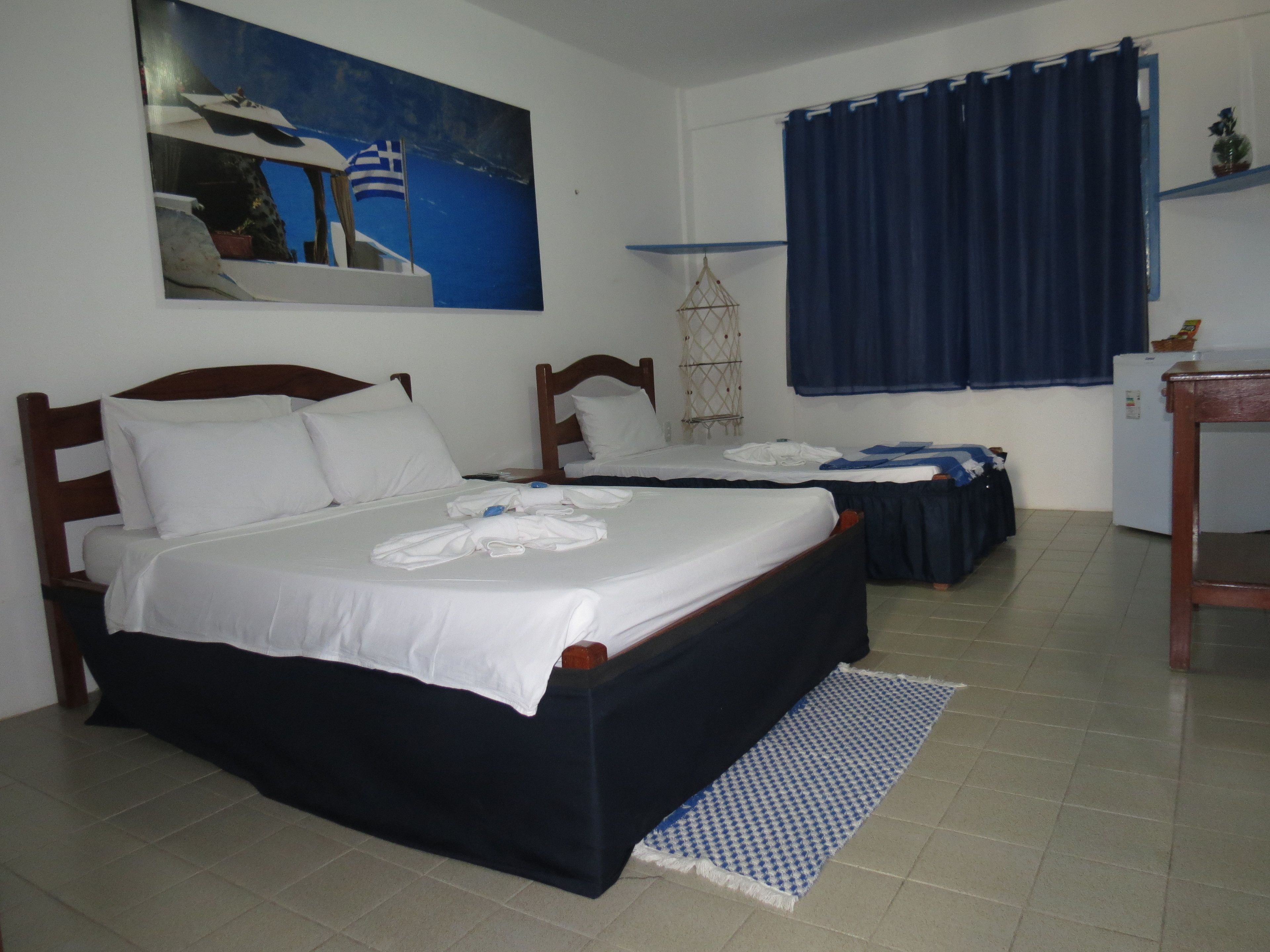 A hotel room with two beds, a small table, a refrigerator, and a painting on the wall.