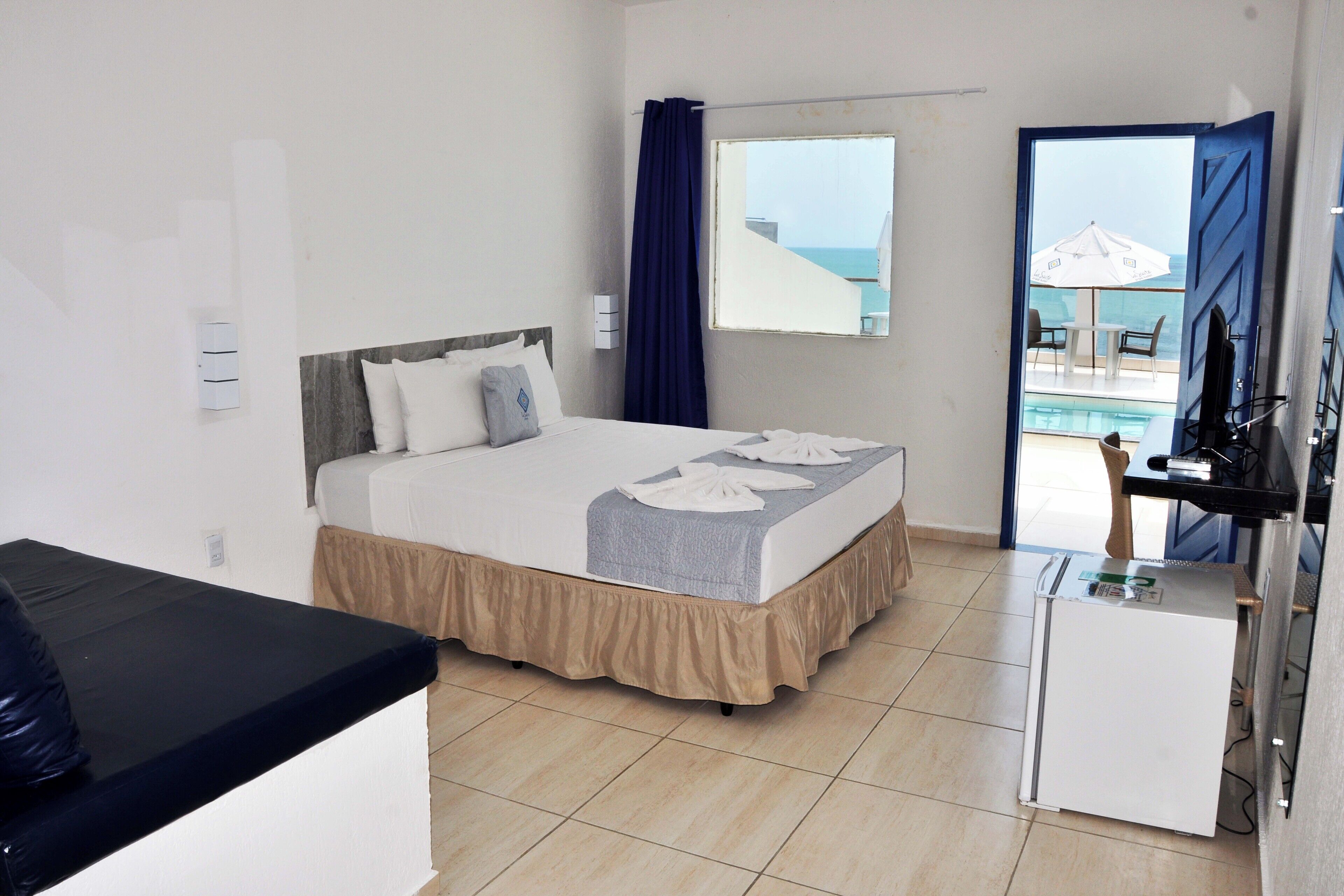 Habitación de hotel con una cama, un escritorio pequeño, una ventana con vista al mar y una puerta que da a un balcón.