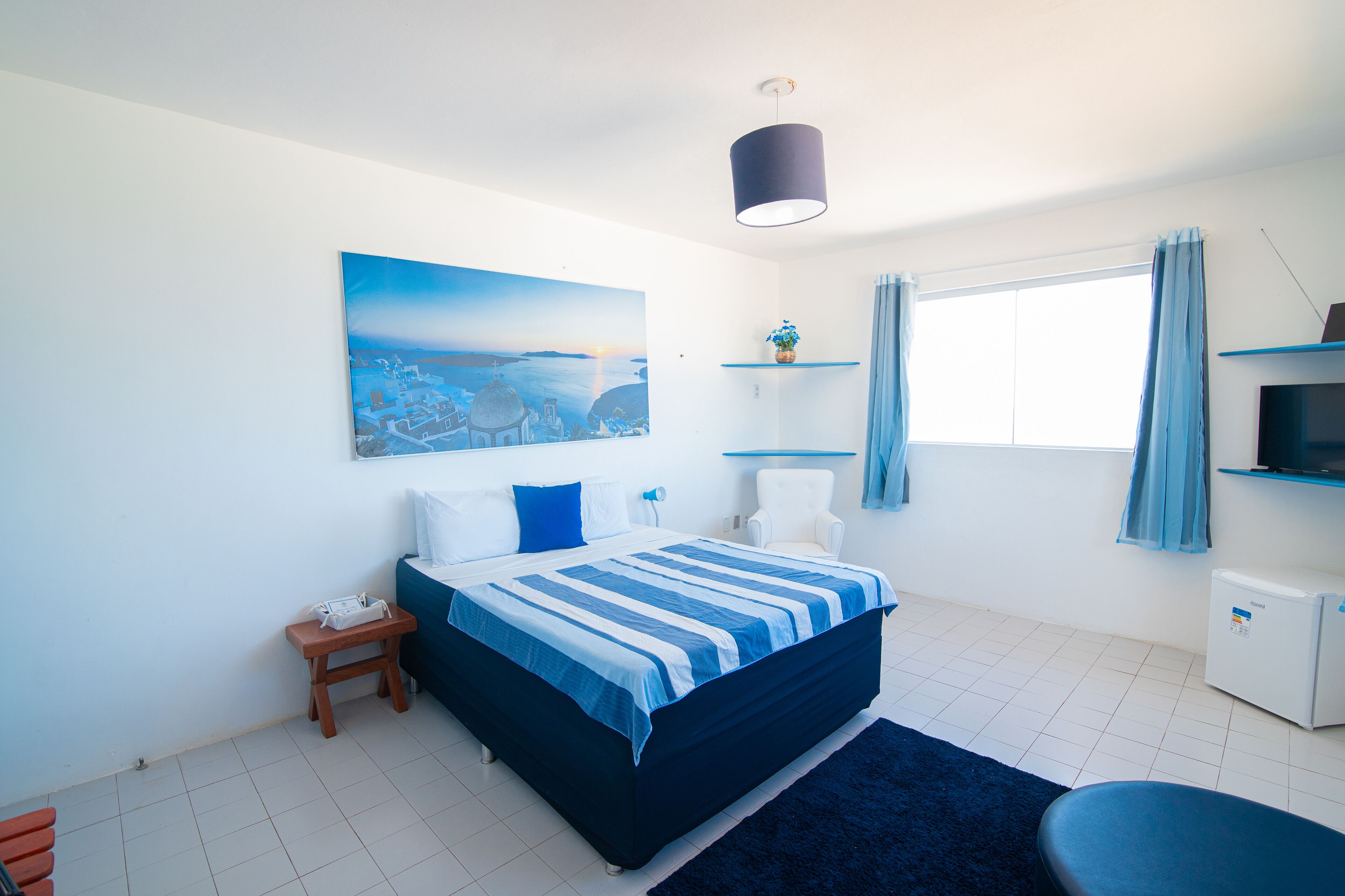 A bedroom with a bed, a nightstand, a chair, a desk, a TV, and a window with curtains.