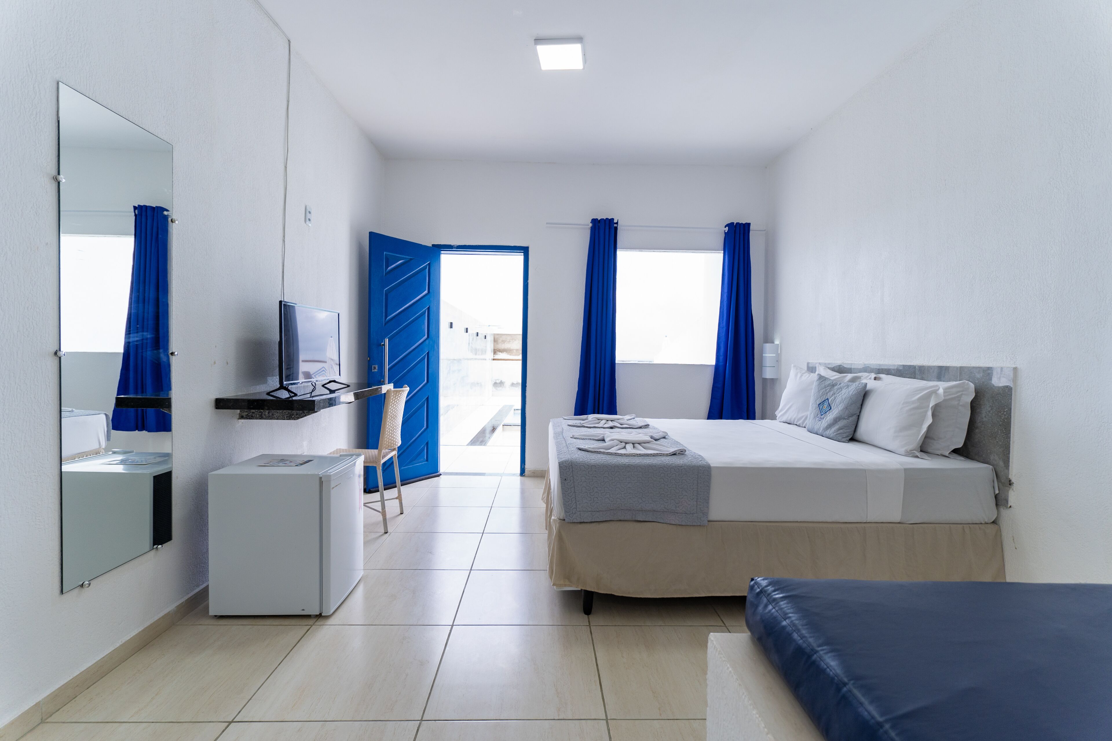 A hotel room with a bed, a small desk, a mirror, and a window with curtains.
