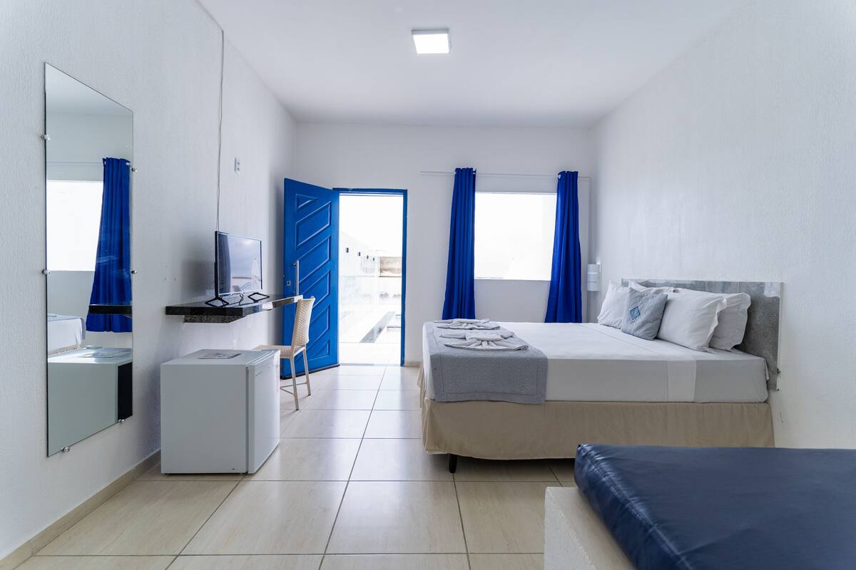 Hotellihuone, jossa on sänky, pieni työpöytä, peili ja ikkuna, jossa on verhot.