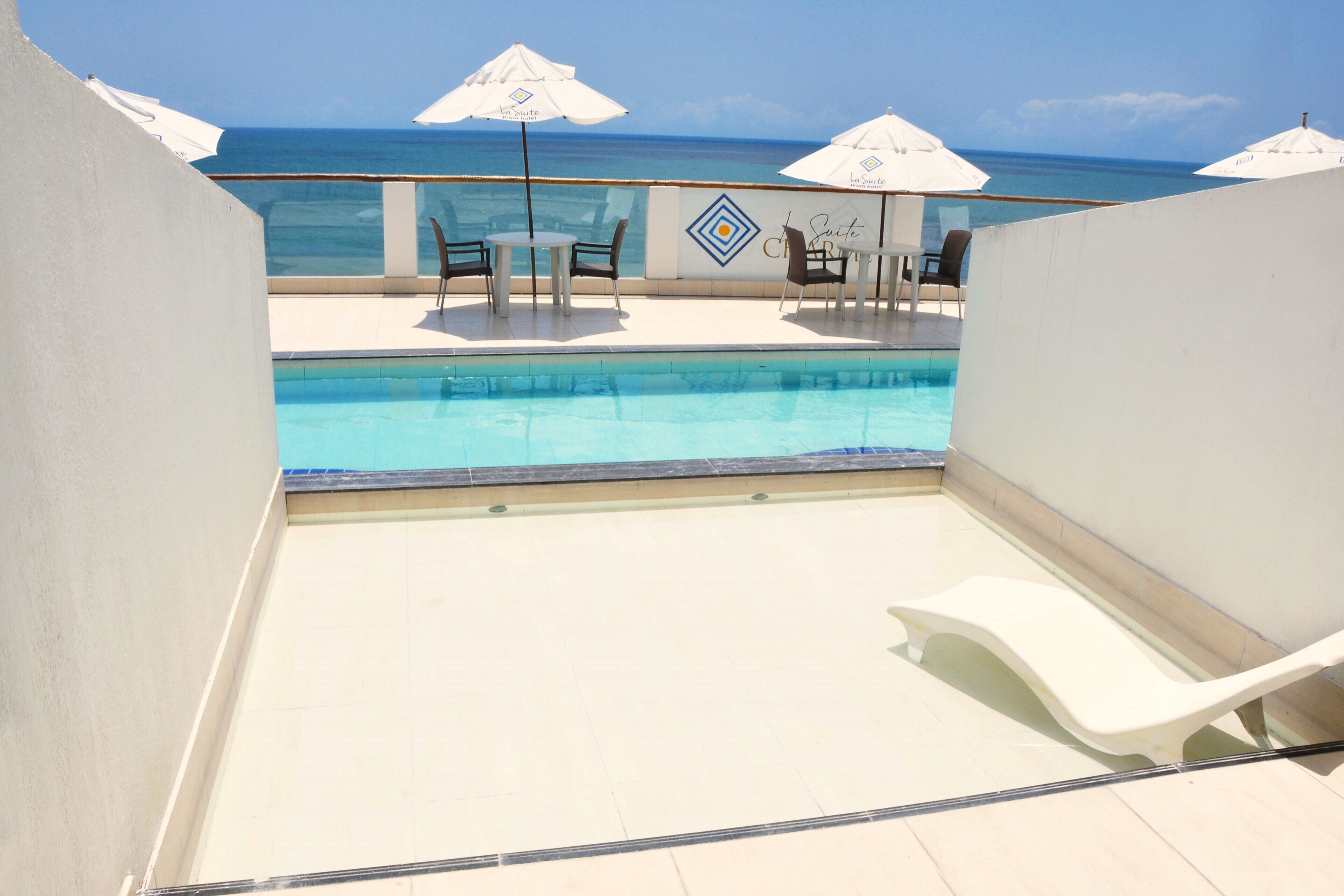 Zona de piscina con vista al océano, sillas reclinables blancas y sombrillas.