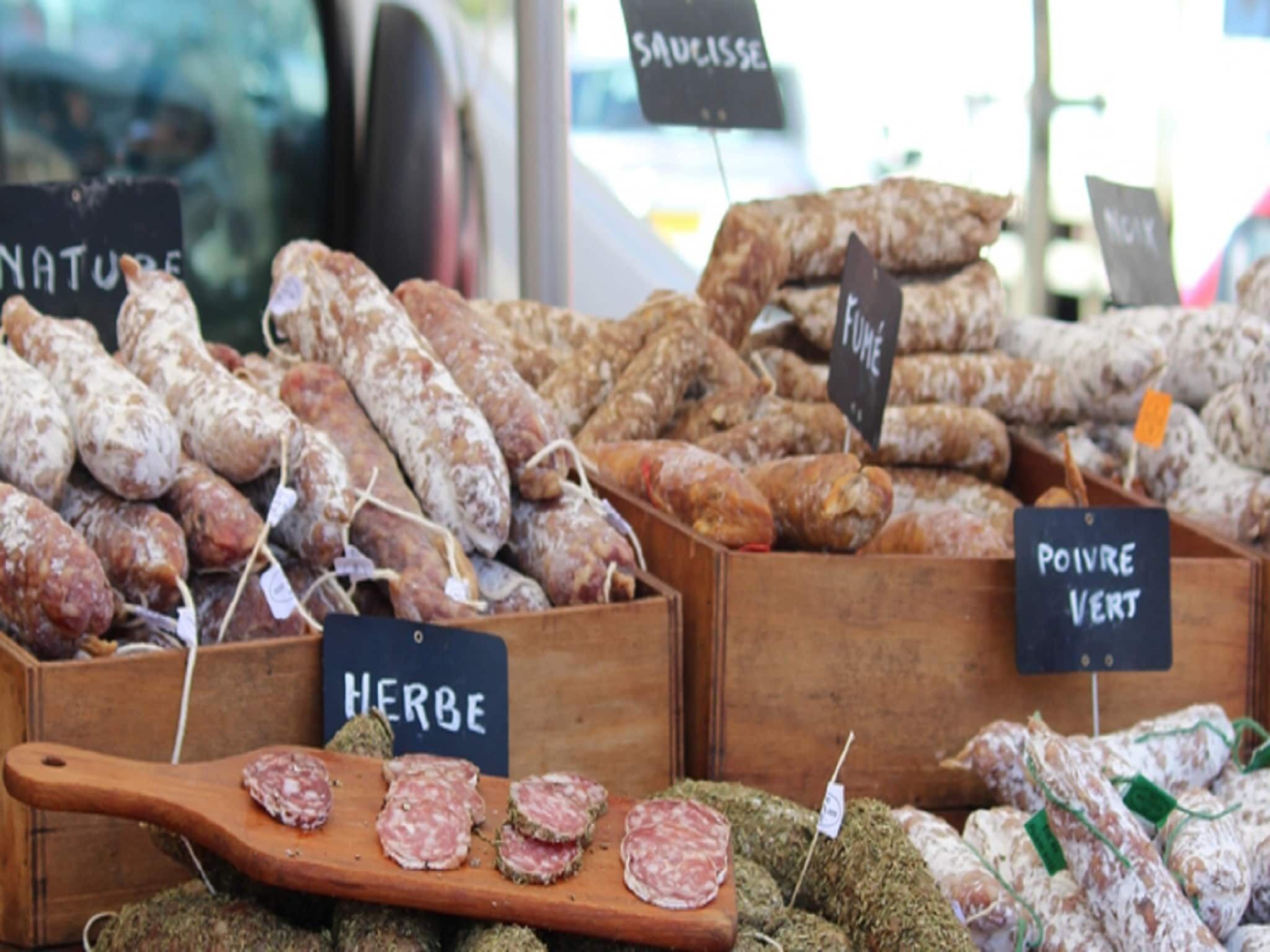 A variety of cured meats displayed in wooden boxes with labels indicating types like 'SAUCISSE' and 'POIVRE VERT'.