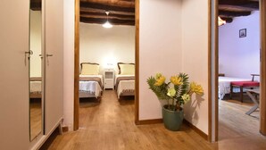 A hallway leading to a bedroom with two beds, a wooden ceiling, and a potted plant.