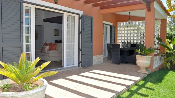 A covered patio area with a stone floor, a seating area with a table and chairs, and a potted plant.