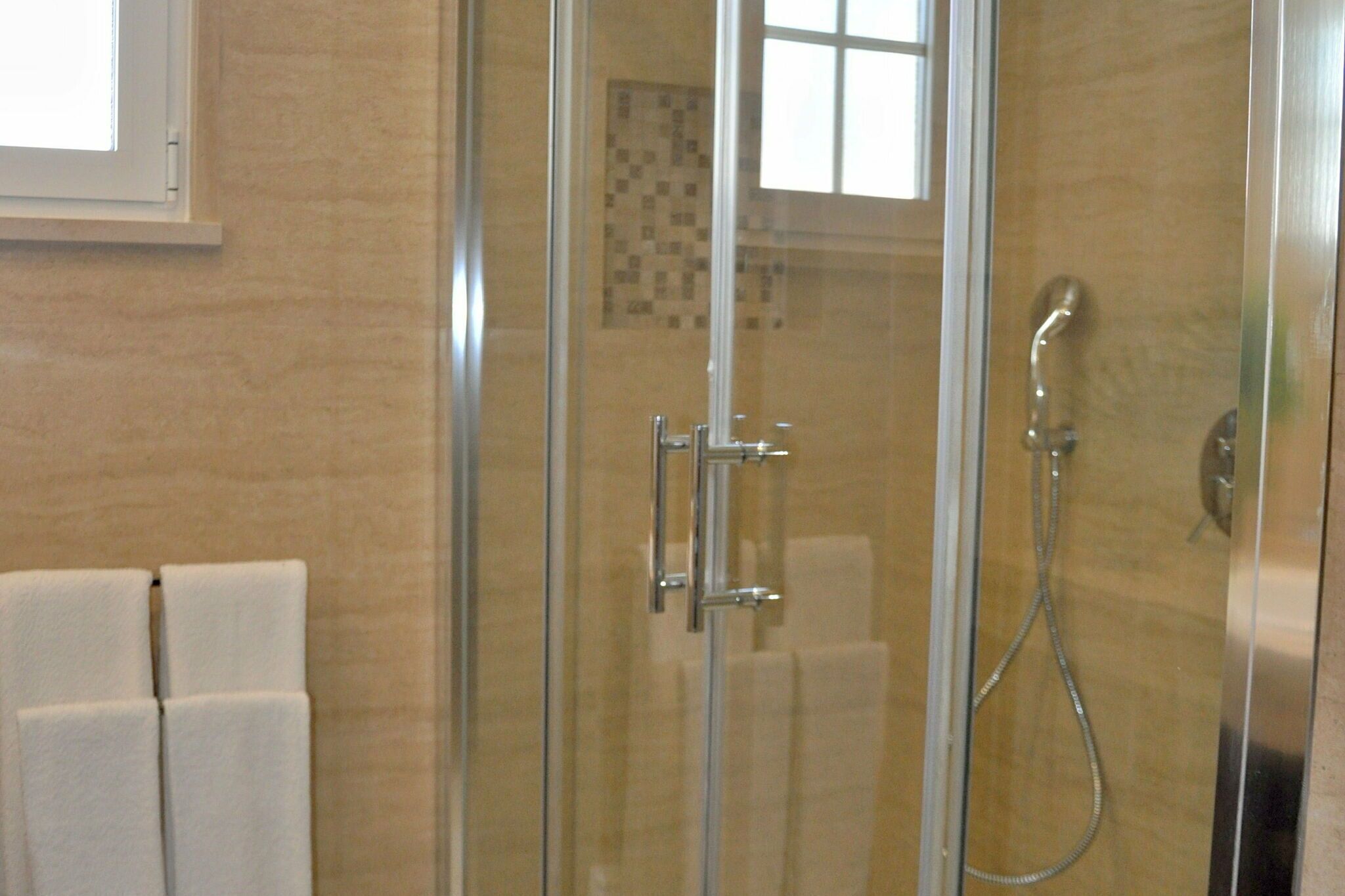 A glass-enclosed shower with a handheld showerhead and a wall-mounted faucet.