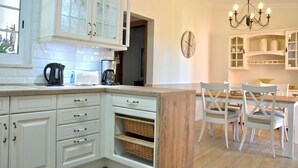A kitchen with white cabinetry, a wooden island, and a dining area with white chairs and a chandelier.