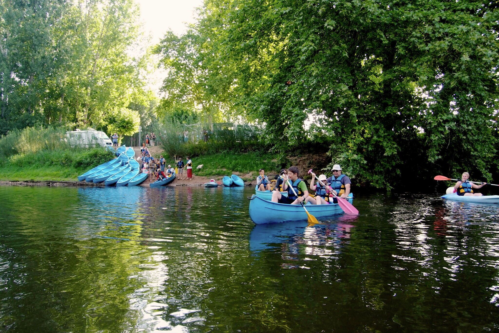 A group of people in kayaks on a calm river surrounded by lush greenery.