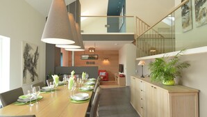 A modern dining area with a long table set for a meal, a staircase, and a living area in the background.